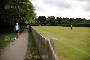 A man walks a dog on a path as people play croquet at Chester Croquet Club in Westminster Park, following the outbreak of the coronavirus disease (COVID-19), Chester, Britain, June 12, 2020. REUTERS/Molly Darlington
